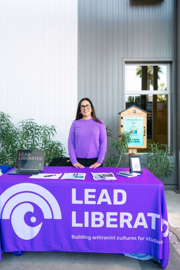 Amber Saberton Stands Behind A Lead Liberated Table