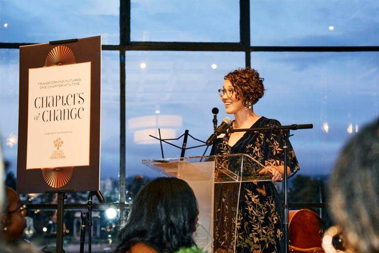 Cassie Perham Standing On A Stage Speaking Into A Microphone
