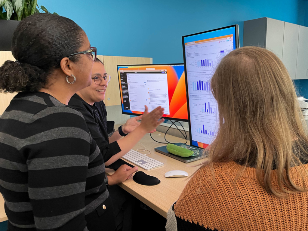 Un grupo de mujeres se reúne en torno a pantallas de ordenador para examinar gráficos de datos en una oficina.